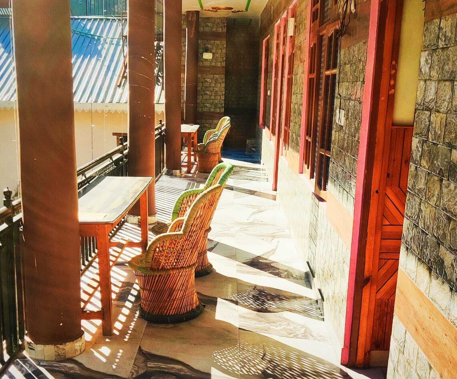 A covered outdoor seating area with wicker chairs and a table, stone walls, and a view of the building's exterior.