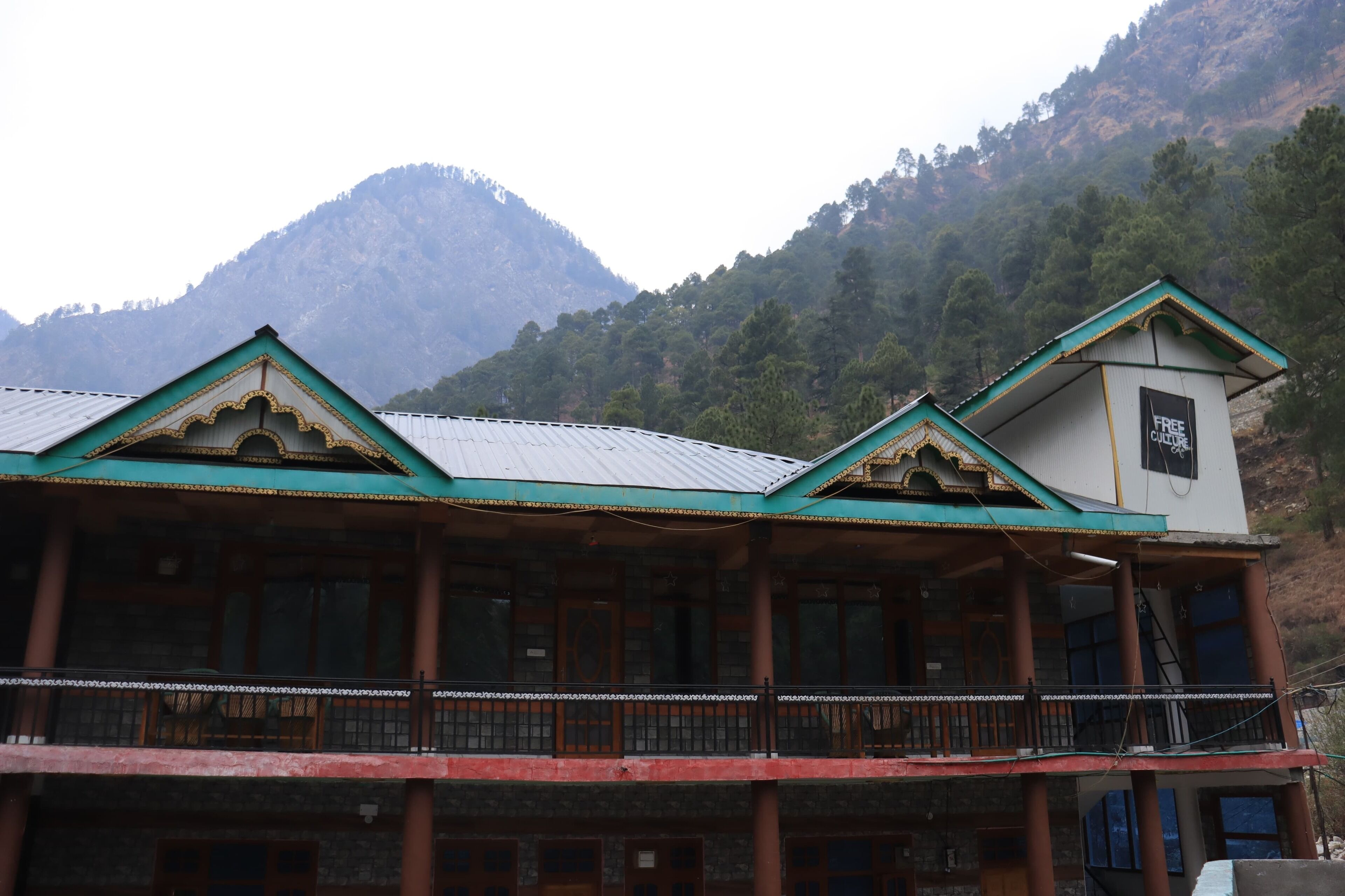 A traditional building with a green roof and multiple balconies, set against a mountainous backdrop.