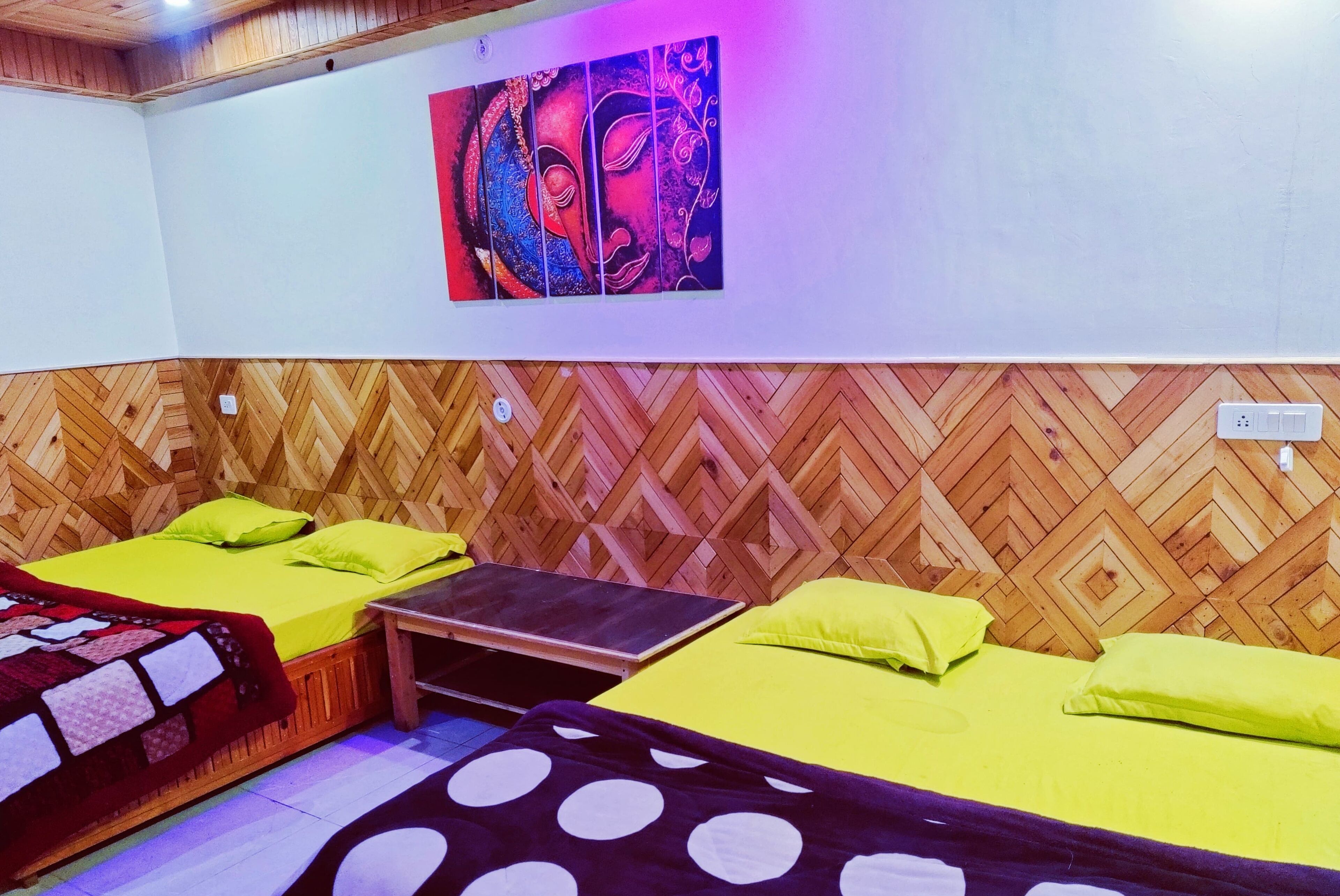 Una habitación con dos camas, cada una con una colcha y almohadas verdes, un muro de madera con estampado en espiga y un cuadro abstracto y colorido sobre las camas.