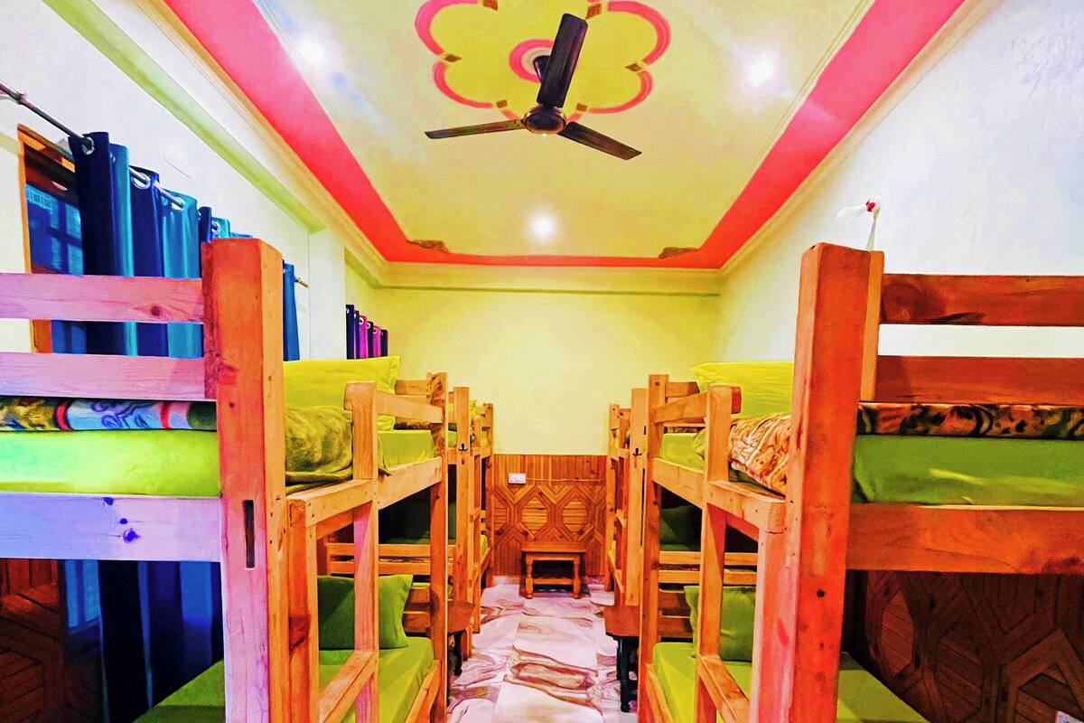 A room with bunk beds arranged in a central aisle, wooden headboards, and a ceiling fan.