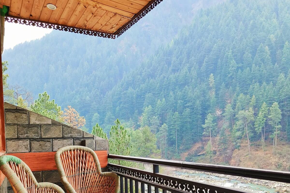 A balcony with wicker chairs and a wooden table, overlooking a mountainous landscape.