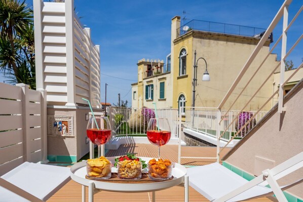 Une terrasse avec une table dressée pour deux personnes, agrémentée d’en-cas et de verres de vin rouge, offrant une vue sur le paysage urbain et ses bâtiments historiques.