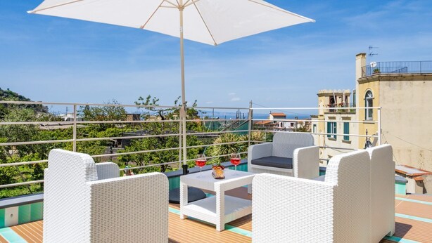 A rooftop terrace with wicker furniture, a table with drinks, and a large umbrella.