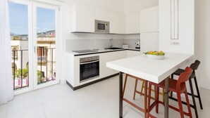 A modern kitchen with white cabinets, a built-in oven, a microwave, and a large island with bar stools.