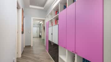 A hallway with a wooden floor, white walls, and a pink storage unit with shelves.