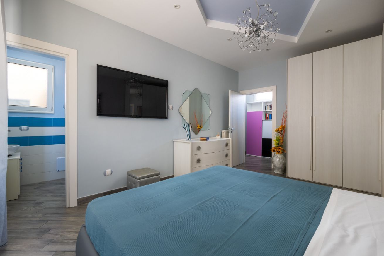 A bedroom with a bed, a TV, a dresser, a mirror, and a window.