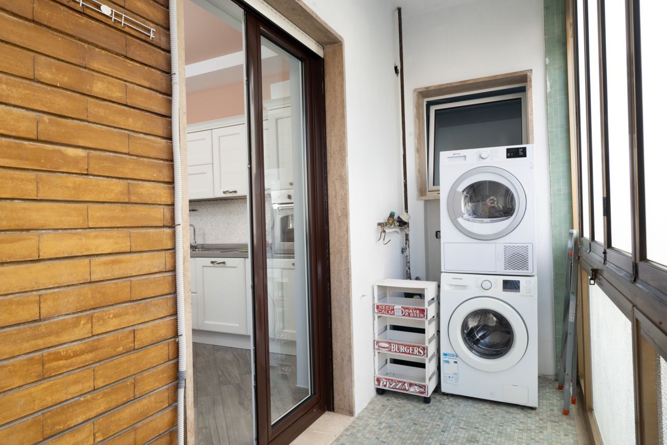 A laundry area with stacked washers and dryers, a sliding glass door leading to a kitchen, and a small shelf with pizza boxes.