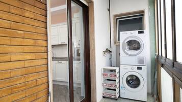 A laundry area with stacked washers and dryers, a sliding glass door leading to a kitchen, and a small shelf with pizza boxes.