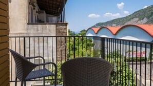 A balcony with wicker chairs, a building with a red roof, and a mountainous backdrop. - Partenope – Elegant Design Apartment in the Heart of Sorrento Coast (Piano di Sorrento)