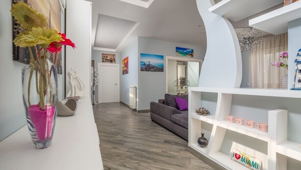 A modern living room with a grey sofa, white shelves, and a vase with flowers. - Partenope – Elegant Design Apartment in the Heart of Sorrento Coast (Piano di Sorrento)