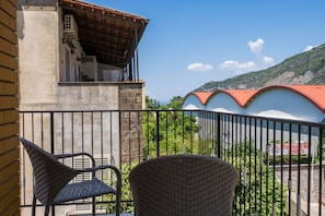 Un balcone con sedie in vimini, un edificio con tetto rosso e montagne sullo sfondo.