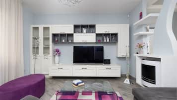 A modern living room with a flat-screen TV, white cabinetry, a glass coffee table, and a fireplace.