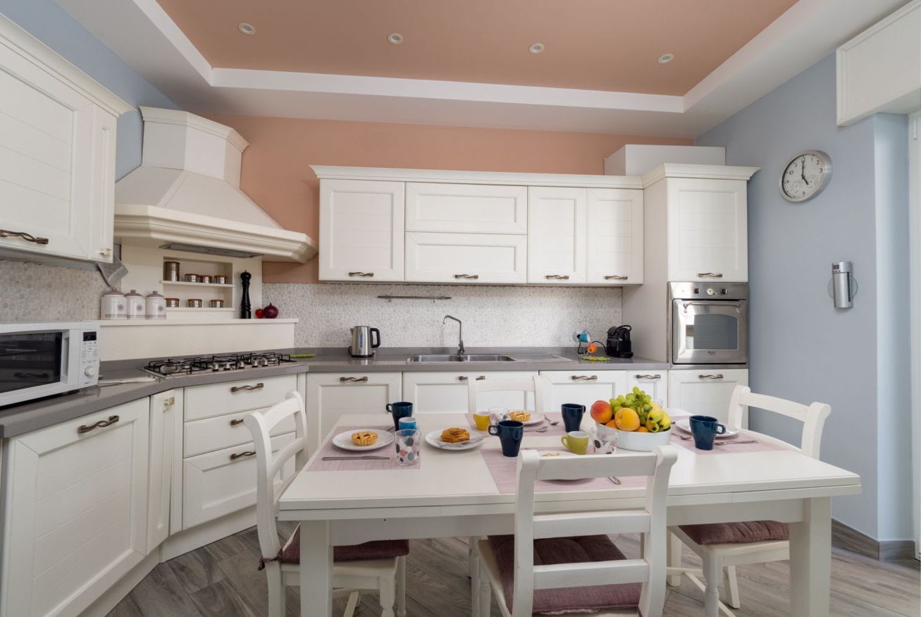 A kitchen with white cabinets, a microwave, a stove, and a sink. There is a dining table with chairs and a clock on the wall.