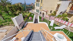 Una terraza con una escalera que lleva a un espacio en la azotea, rodeada de un jardín y edificios.