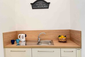 A kitchen with a sink, a kettle, and a fruit basket.