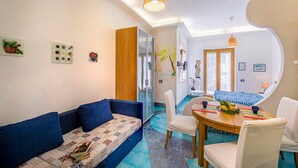 Una sala de estar moderna con sofá, mesa de comedor y sillas, una escalera que sube a otro nivel, y un ventanal con luz natural.