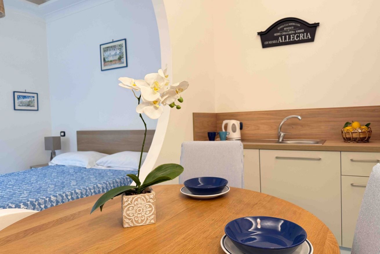 A hotel room with a bed, a small dining table with blue bowls, a potted orchid, and a sign on the wall.