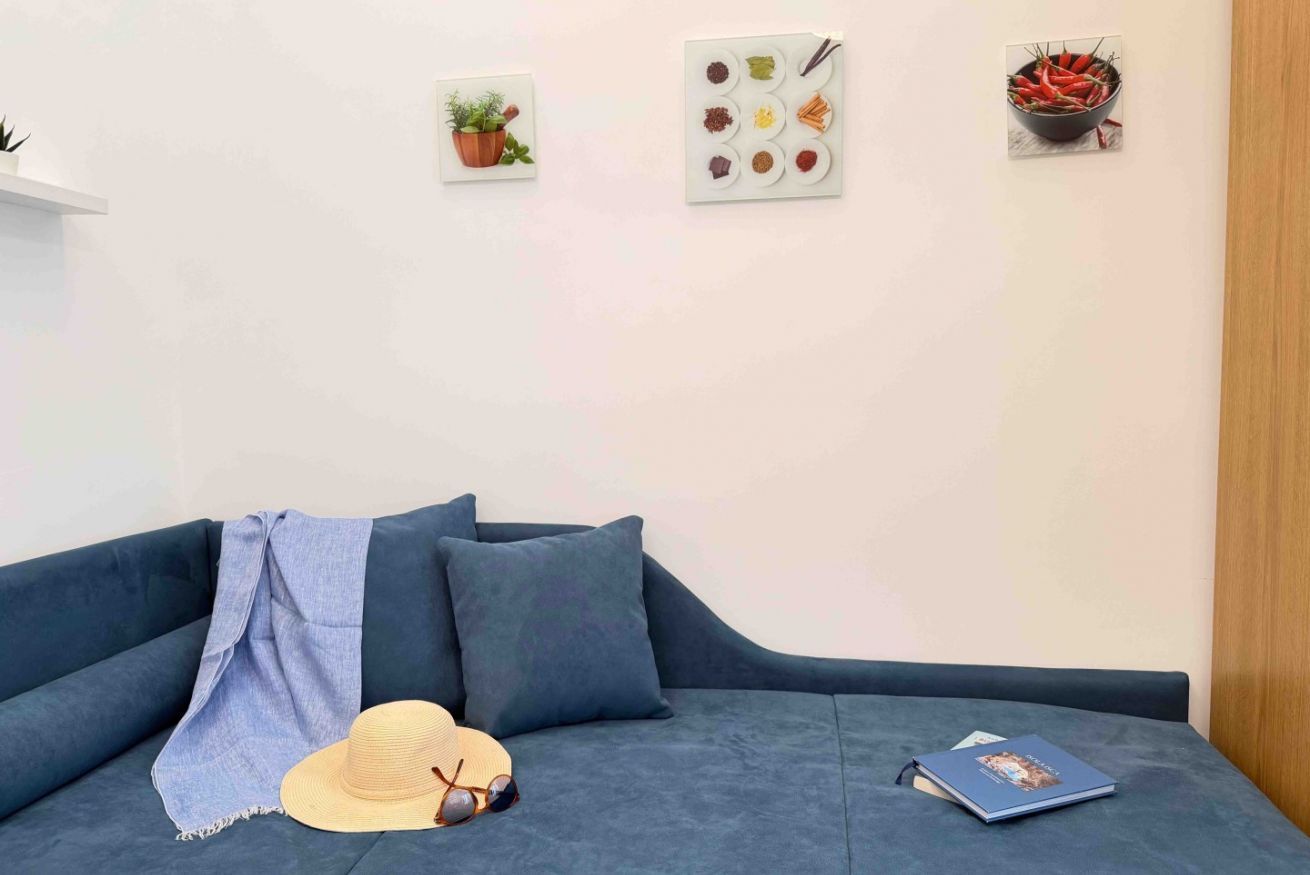 A modern living room with a blue sofa, a hat, sunglasses, and a book on it. There are wall-mounted pictures of plants and food.