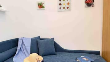 A modern living room with a blue sofa, a hat, sunglasses, and a book on it. There are wall-mounted pictures of plants and food.