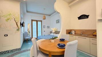 A room with a dining table, chairs, a bed, a kitchen area, and a wall with a sign.