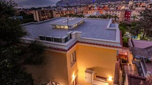 Un edificio residencial con techo plano, balcón y vista a una ciudad costera al atardecer.