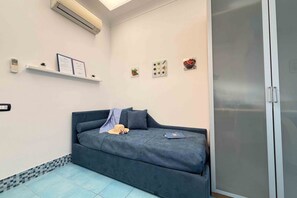 Una habitación con un sofá azul oscuro, una mesita pequeña, aire acondicionado instalado en la pared y un ventanal corredero.