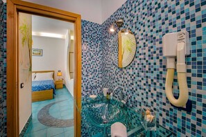 Ein Badezimmer mit einem Glaswaschbecken, einem Spiegel und einem Handtrockner.