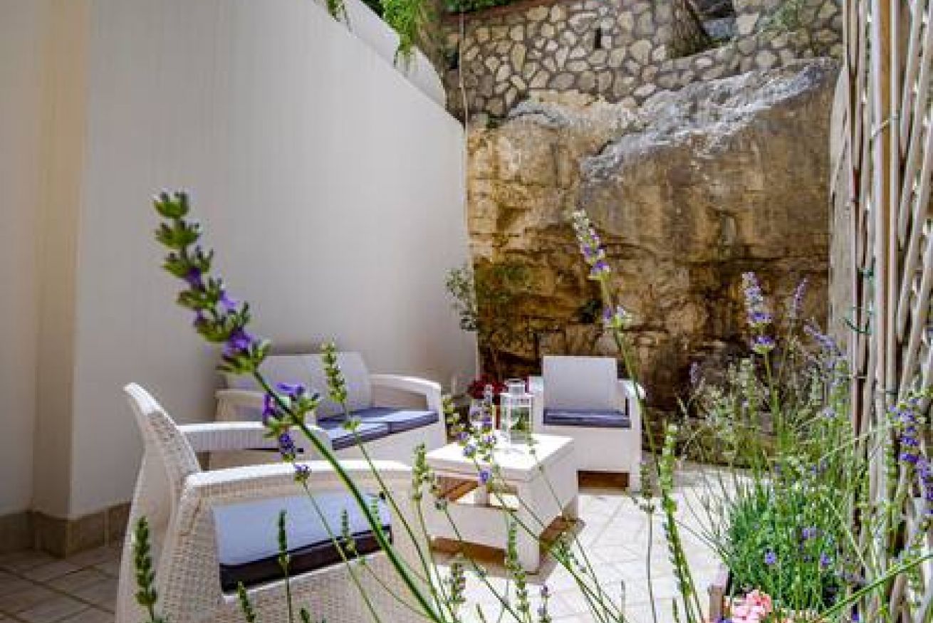 A patio with white wicker furniture, a stone wall, and purple flowers.