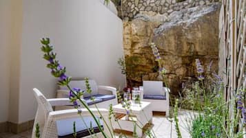 A patio with white wicker furniture, a stone wall, and purple flowers.