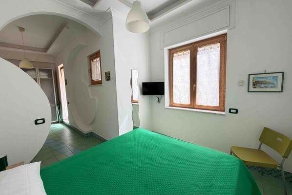 A room with a bed, a television, a window, and a chair.