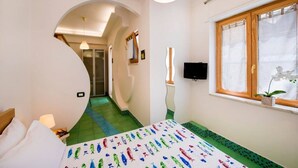 Un dormitorio con cama, televisor, ventana con cortinas y pasillo que conduce a otra habitación.