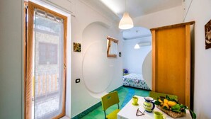 Una habitación pequeña e iluminada con una mesa de comedor, sillas, un ventanal con vistas y una puerta que da a otra habitación.