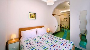 Un dormitorio con una cama, mesitas de noche, una lámpara, un cuadro enmarcado en la pared y un espejo curvo.
