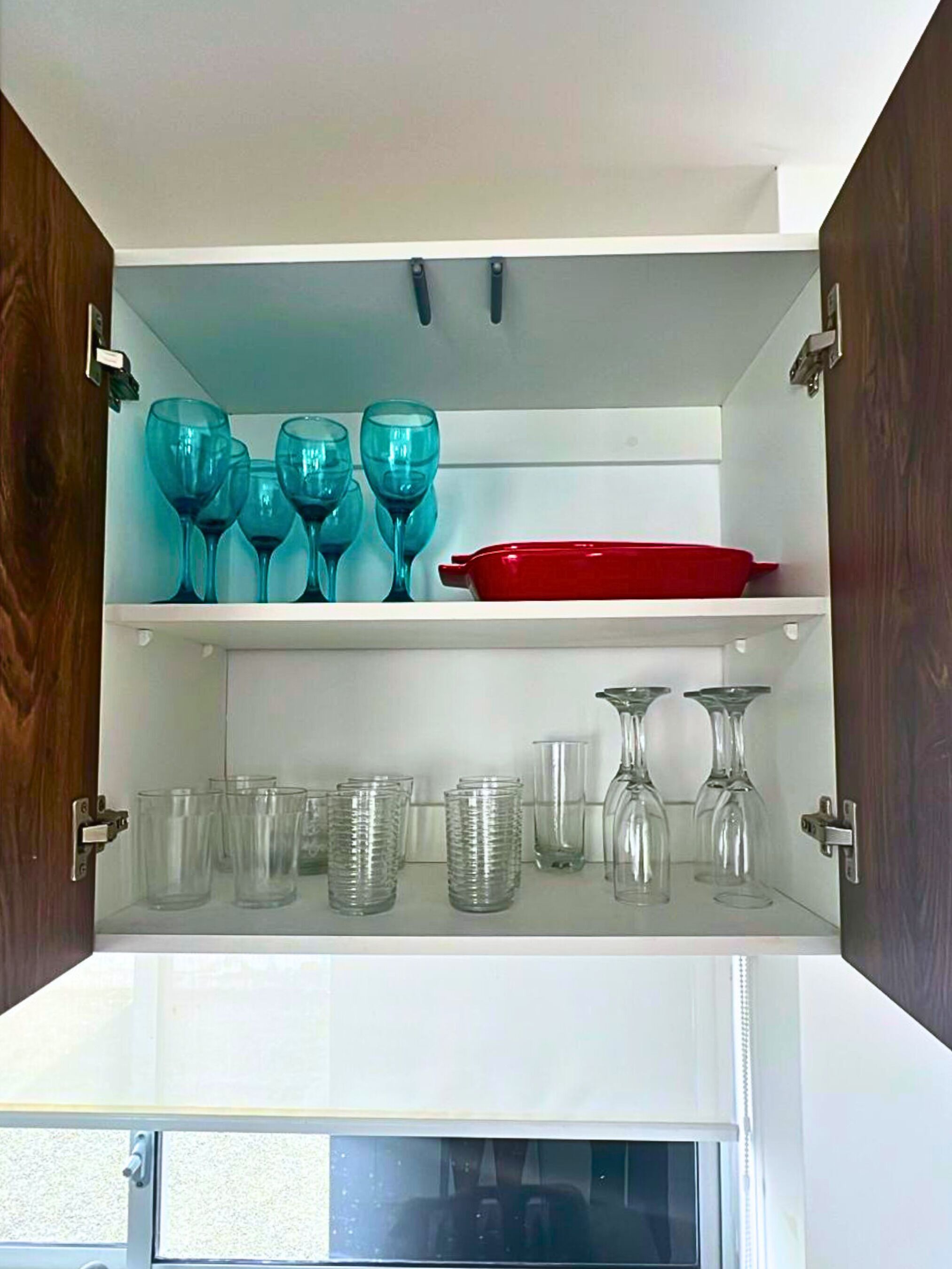 Un meuble de cuisine avec, sur l’étagère supérieure, des verres à vin de couleur turquoise et, sur l’étagère inférieure, des verres à eau transparents.