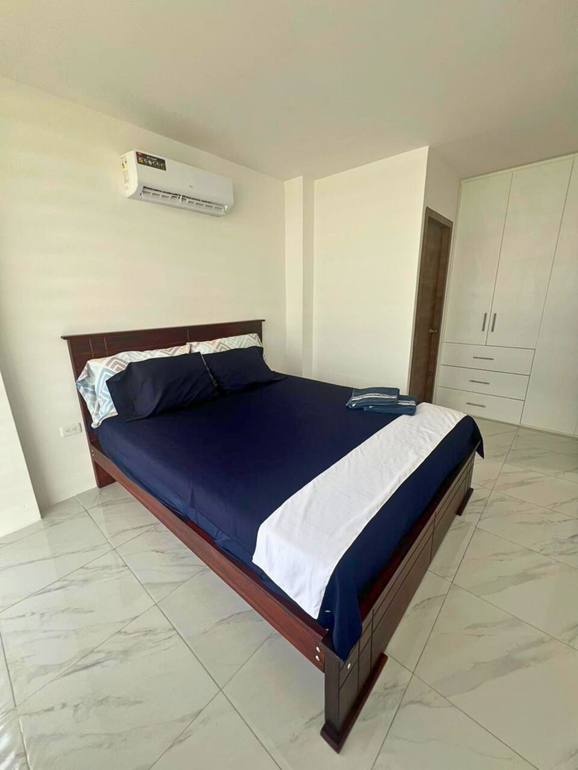 Un dormitorio con cama, aire acondicionado, armario y suelo de baldosas.