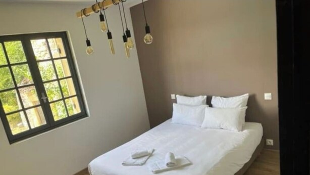 A neatly made bed with white linens and towels, a window with blinds, and a hanging light fixture. - House Vezac (Vezac)