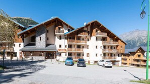 A multi-story hotel with balconies, a stone facade, and a view of mountains.