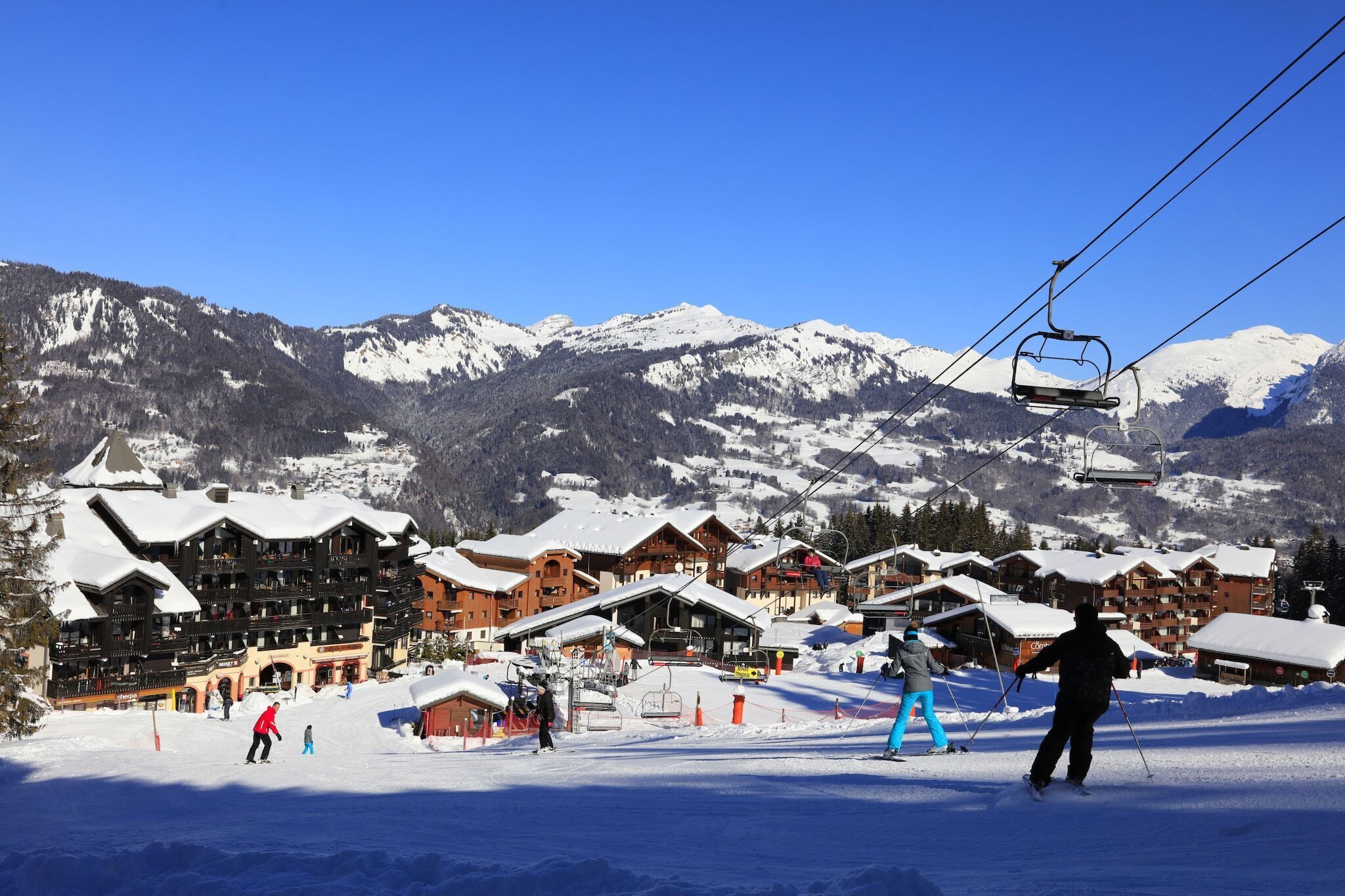 A ski resort with wooden chalets, a ski lift, and snow-covered mountains in the background.