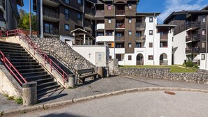 A multi-story hotel with a stone staircase, balconies, and a paved courtyard. - Apartment in Morillon at Ski Slope (Morillon)