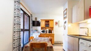 A compact kitchen with wooden cabinets, a microwave, and a washing machine. - Apartment in Morillon at Ski Slope (Morillon)