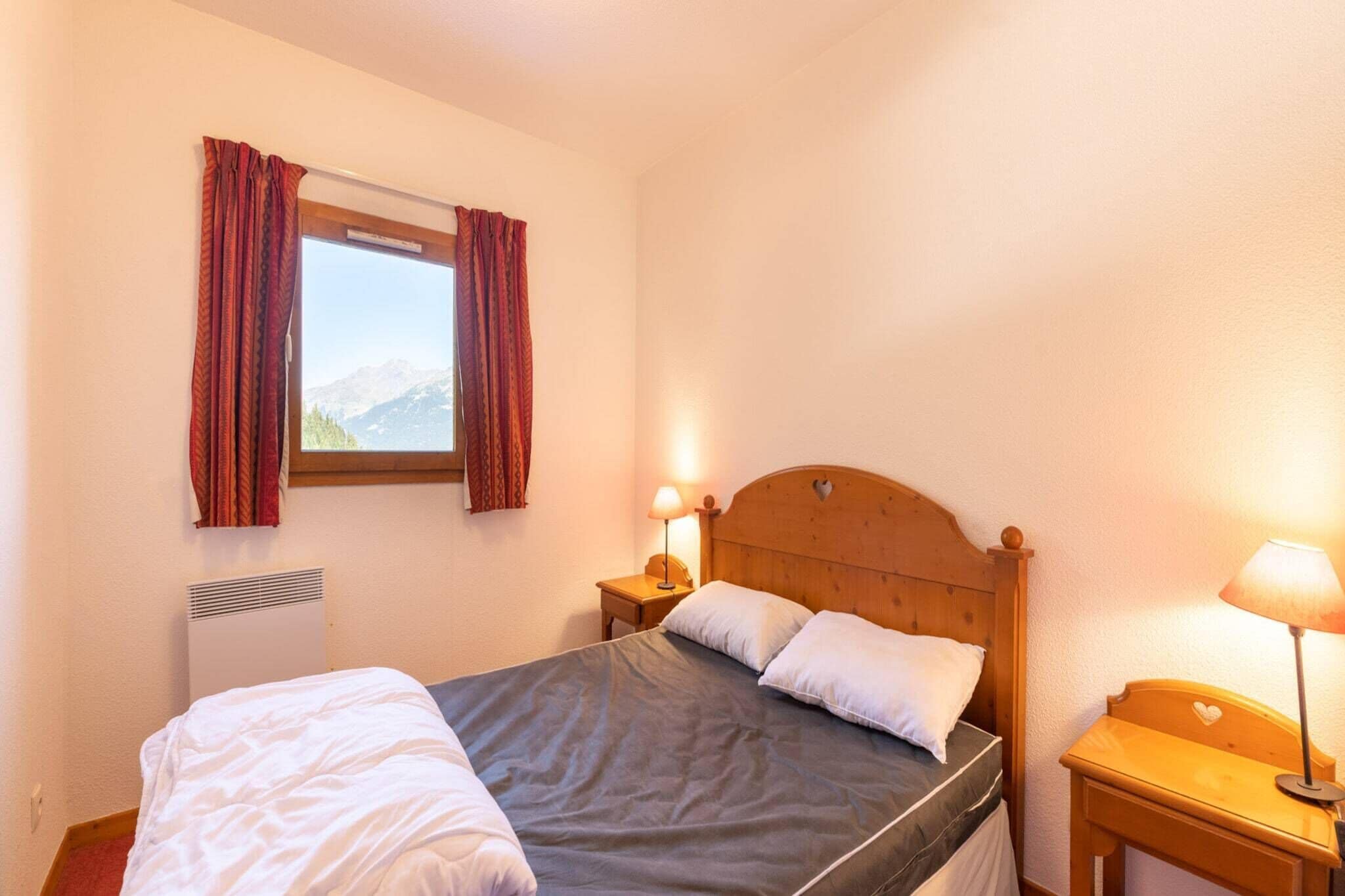 Een slaapkamer met een bed, een raam met gordijnen, een nachtkastje met een lamp en een verwarming.