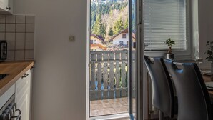 A kitchen with a wooden countertop, a clock, and a view of a balcony with a wooden railing and a potted plant. - Mountain Nature Apartment with Balcony in Savinja Valley (Mozirje)
