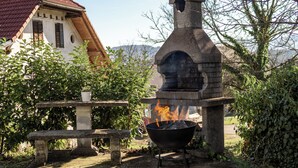 A stone outdoor oven with flames, a stone bench, and a potted plant. - Mountain Nature Apartment with Balcony in Savinja Valley (Mozirje)