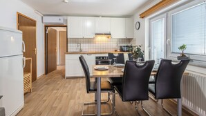 A modern kitchen with white cabinets, a wooden countertop, and a dining area with black chairs. - Mountain Nature Apartment with Balcony in Savinja Valley (Mozirje)