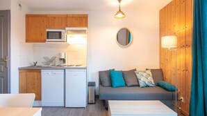 A compact living space with a kitchenette, a sofa with cushions, a small table, and a mirror on the wall. - Apartment in Saint-Sorlin near Ski Slopes (Saint-Sorlin-d´Arves)