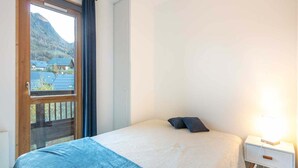 A bedroom with a bed, a nightstand, a window with a view of houses and mountains. - Apartment in Saint-Sorlin near Ski Slopes (Saint-Sorlin-d´Arves)