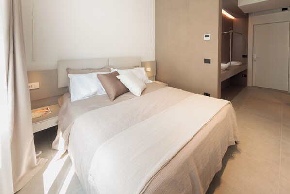A modern bedroom with a large bed, bedside tables, a built-in bench, and a walk-in closet.