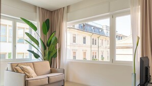 Una sala de estar moderna con un sofá color crema, una planta verde grande y un televisor sobre una mesa blanca.