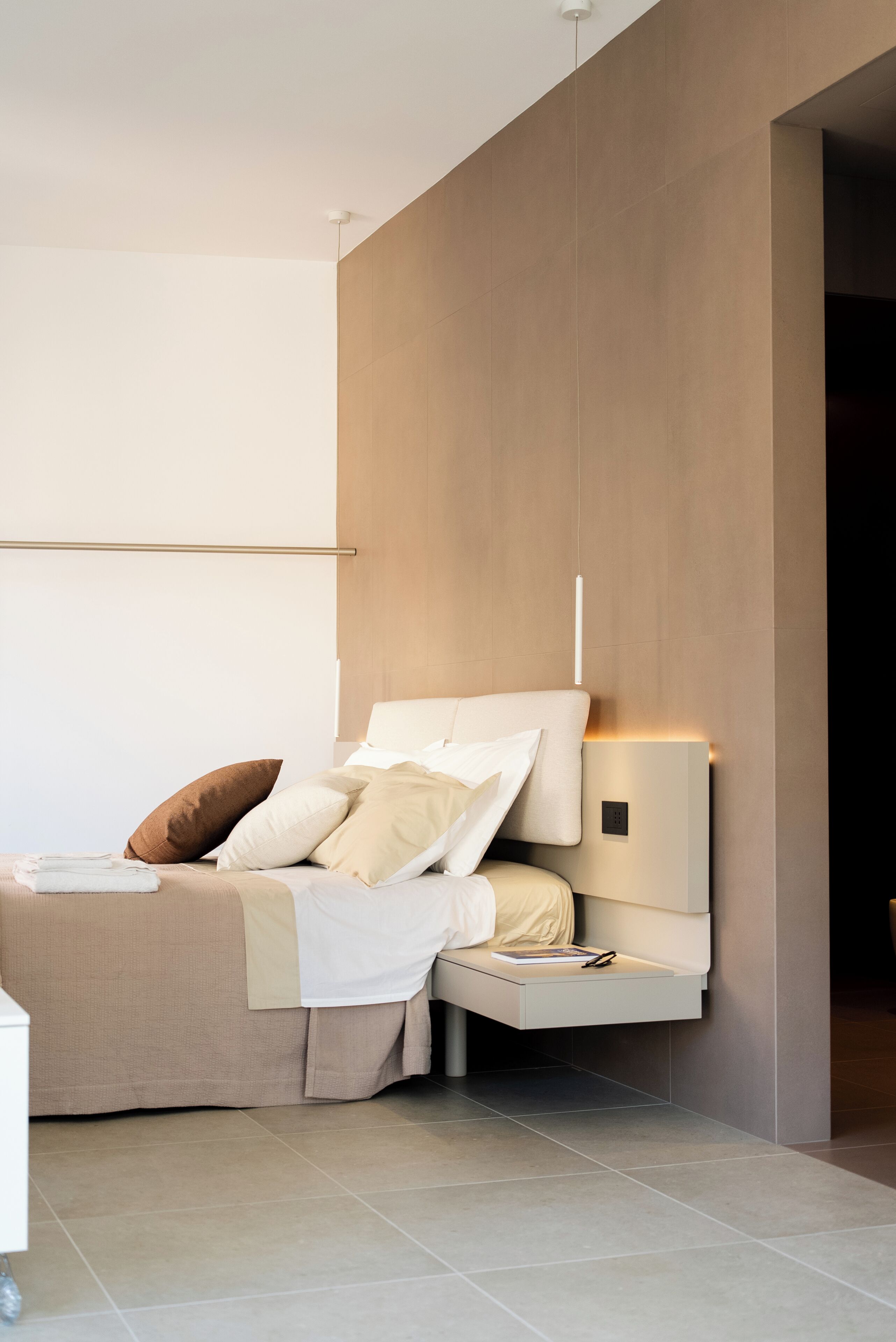 A modern bedroom with a bed, bedside table, and a wall-mounted light fixture.
