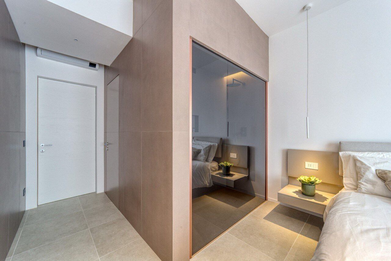 A modern bedroom with a large mirror, a bed with a headboard, a bedside table with a plant, and a door with a handle.